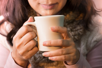 Close up of woman hands holding a cup of coffee. 
Female in winter fashion clothes enjoying hot drink with smiling face,selective focused.