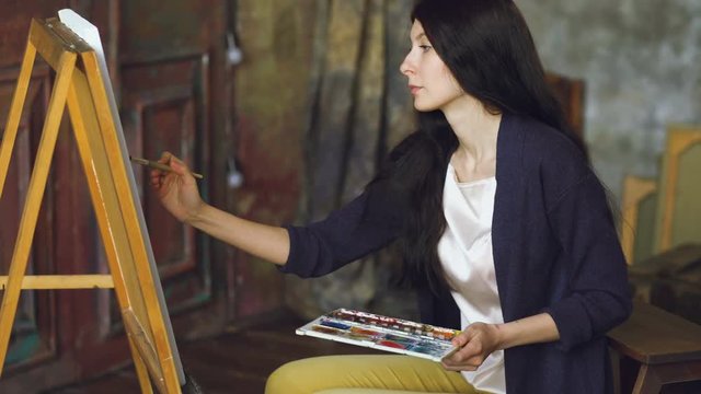 Young woman artist draw pictrure with watercolor paints and brush on easel canvas