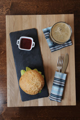 Burger, beer and berry sauce in white gravy boat on a slate base, glass and cutlery served on a wooden board,