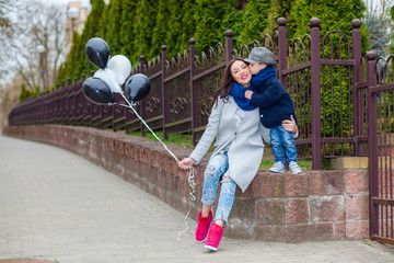 Portrait of fashionable baby boy and his gorgeous mother among balloons. little boy hugs his mother...