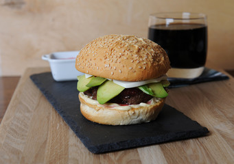 Burger, beer and berry sauce in white gravy boat on a slate base, glass and cutlery served on a wooden board,