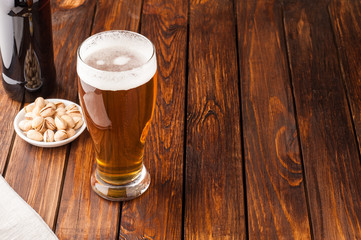 glass of light cold frothy beer, nuts, bottle, old wooden table