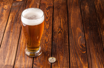 glass of light cold frothy beer,cap old wooden table