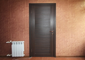 dark wooden closed door close-up on the wall with red vintage wallpaper and white battery radiator