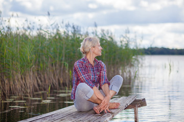 middle-aged woman on the pier. Concept joyful elderly. Portrait of happy middle aged woman sitting on the beach.