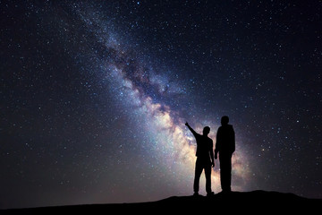 Silhouette of a father and a son who pointing finger in night starry sky on the background of Milky...