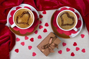 Two cups with coffee with drawn hearts on the foam gift box and red paper hearts. Top view. Romantic background.