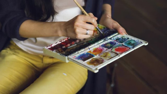 Young woman artist draw pictrure with watercolor paints and brush mixing colors closeup