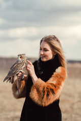 Beautiful woman in a fur coat with an owl on his arm. Blonde with long hair in nature holding a owl. Romantic delicate image of a girl