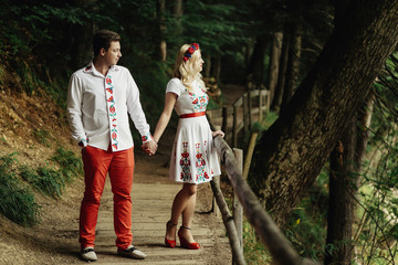 Naklejka na ściany i meble Man and woman in embroidered clothes walk along wooden path in t