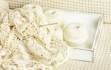 crochet tablecloth, crochet hooks and balls of cotton thread on a white woolen plaid