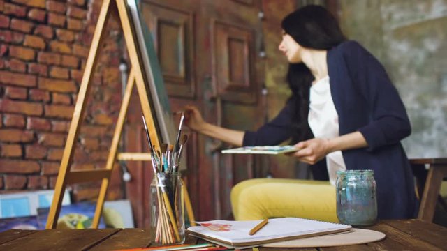 Young woman artist draw pictrure with watercolor paints and brush on easel canvas