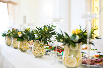 Glass vases with lemons, greenery and yellow flowers stand on ri