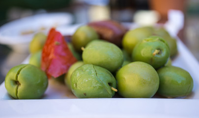 Many marinated olives with herbs and spices in a small plate on the tapas bar table a typical Spanish black and green split olive. With the red touch of a pepper
