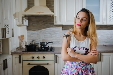 young woman is cooking in the kitchen with joy. She is standing and holding rolling pin and spoon