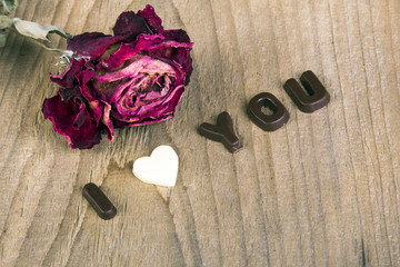 dried rose and chocolate words I LOVE YOU on wooden background