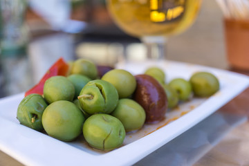 Marinated olives with herbs and spices in a small plate on the tapas bar table a typical Spanish black and green split olive. In the background a blurred beer