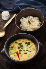 Thai soup and rice in ceramic bowls on dark background.