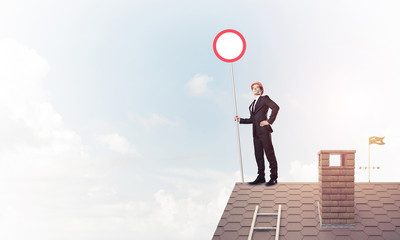 Obraz premium Caucasian businessman on brick house roof showing stop road sign