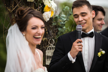 Bride laughs broad while groom sings in the mircrophone with clo