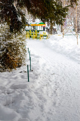 Naklejka premium Snow-covered path under fir trees. In the distance, a colorful children's train. Winter landscape.