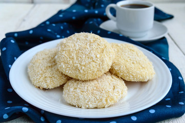 Crispy dietary coconut cookies on a plate and a cup of coffee on a white wooden background. Close up