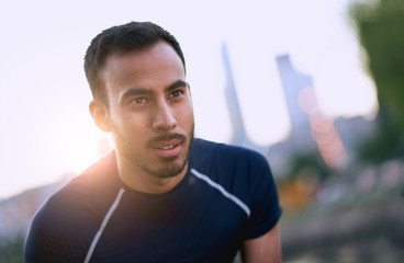 Portrait of active millenial man jogging at dusk with an urban cityscape and sunset in the background