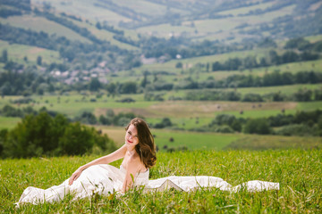 Brunette bride in ivory dress rests on green lawn with great lan