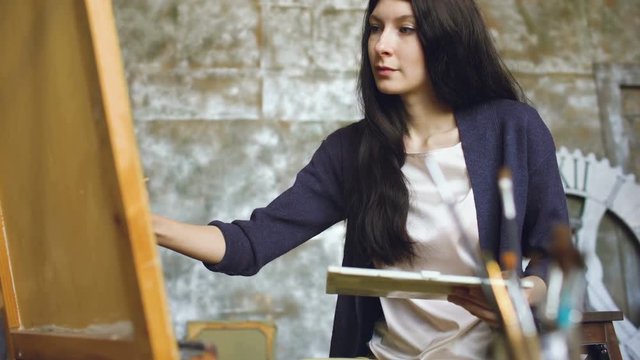 Young woman artist draw pictrure with watercolor paints and brush on easel canvas