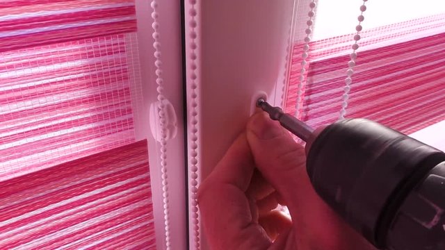 Installing fabric roller blinds. A man fixing plastic bracket on the frame of the window.