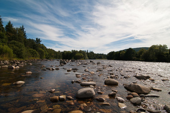 Salmon river in Scotland with pebbled banks and blue sky to background