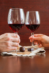 Two glasses of wine on a wooden table. Candies. Hands.