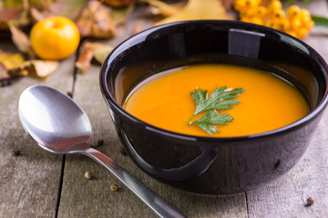 Autumn pumpkin soup in black bowl on natural desk.