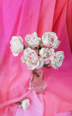 Pale pink roses in a glass vase on a background of pink silk drapes.