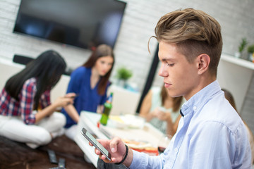 Teenage boy text messaging with blurred friends sitting in the living room at home.