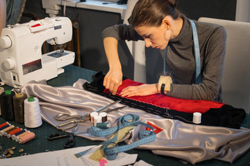 The dressmaker sews fabric with white thread
