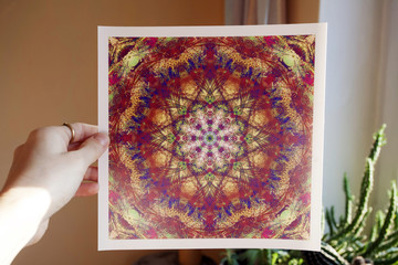 Hand holding abstract mandala picture inside home interior