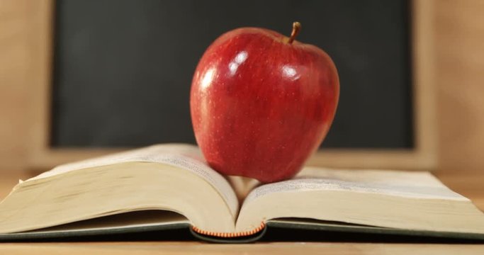 Close up of red apple with open book on a desk