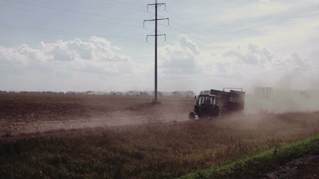 farm tractor with a trailer rides on the field, raising clouds of dust