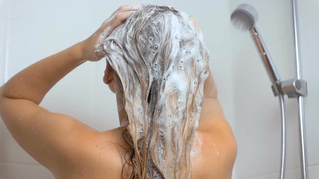 Slow motion footage of woman with long hair applying shampoo at bath