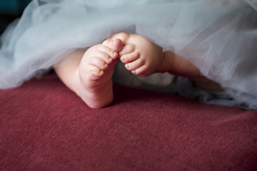 baby feet of a small girl sitting in a blue fashion skirt on dark background