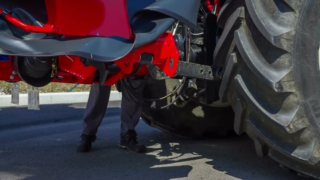 A farmer is standing by a tractor and he is connecting it to a trailor. He needed to fix something.
