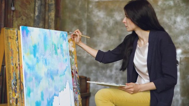 Young woman artist draw pictrure with watercolor paints and brush on easel canvas
