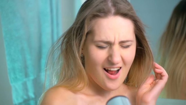 Slow motion footage of beautiful young woman singing to hair dryer at bathroom