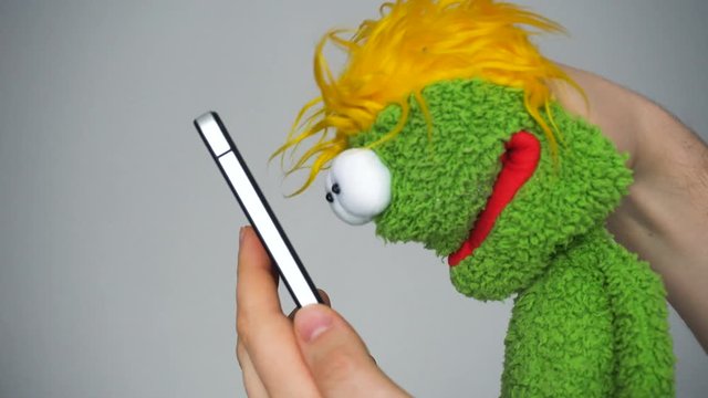 Funny green puppet looking in smartphone