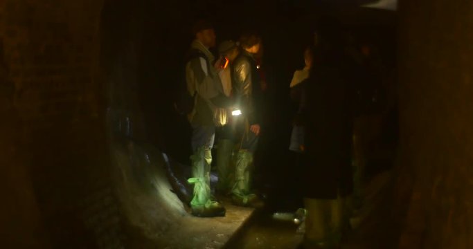 People Are Standing in an Enigmatic Dark Tunnel, and Talking to Each Other, Being Dressed in Green Chemsuit Boots, and Keeping Flashlights in Hands