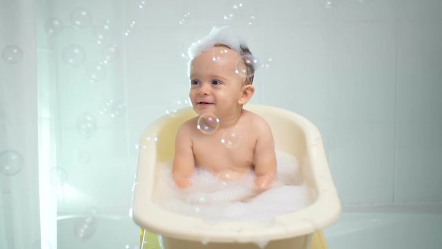 Slow motion footage of cute toddler boy bathing and looking at soap bubbles