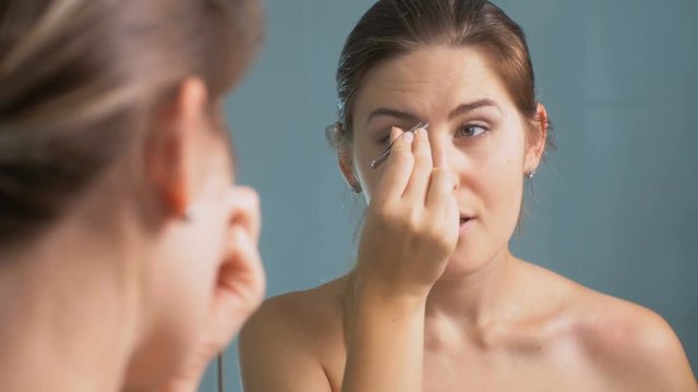 4K closeup footage of beautiful brunette woman shaping her eyebrows at mirror