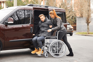 Young woman helping handicapped man to sit in wheelchair