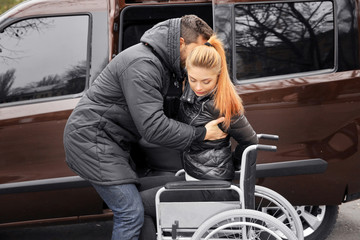 Young man helping handicapped woman to sit in wheelchair